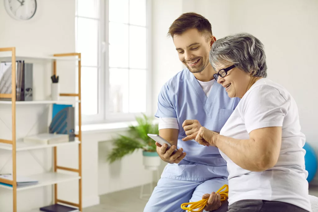 Physical therapist in scrubs showing older woman something on a smart phone.