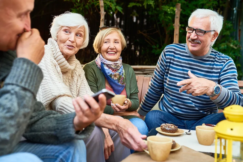 Group of cheerful retirement-age people enjoying time together drinking coffee outdoors in cafe and sharing life stories