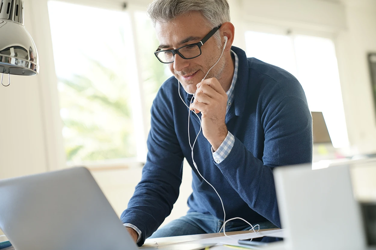 Middle aged businessman in office talking to client on phone with earphones