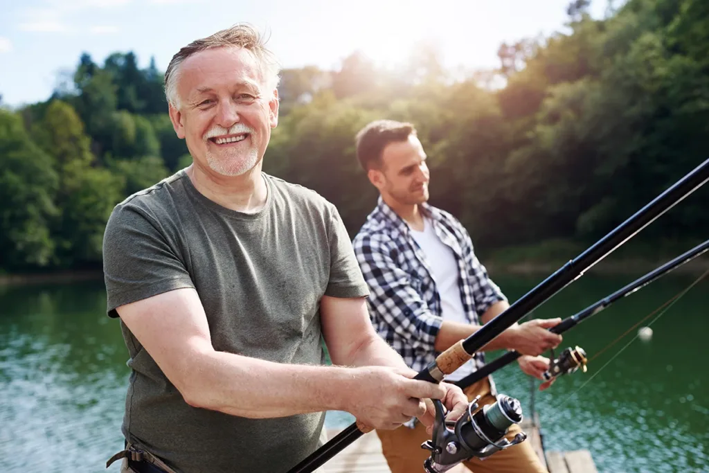 Older man and adult son happily fishing together at the river.