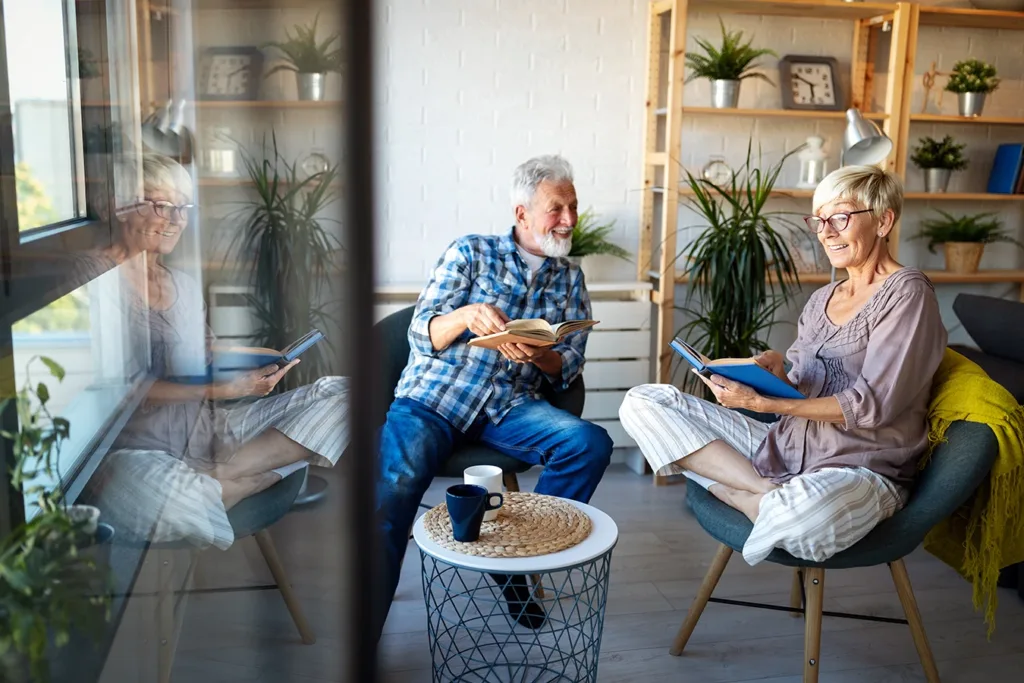 Happy senior couple, husband and wife, sitting in their living room, reading out loud from a book, and drinking coffee