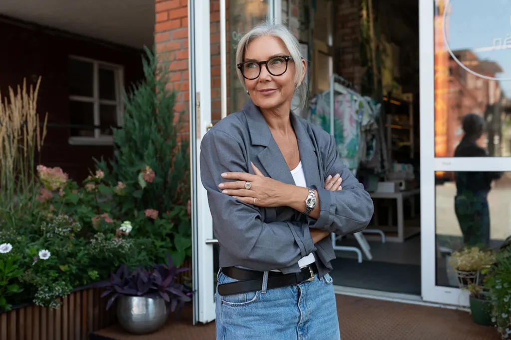 Happy middle aged woman with stylish grey hair dressed in a gray blazer and trendy silver jewelry in an urban environment